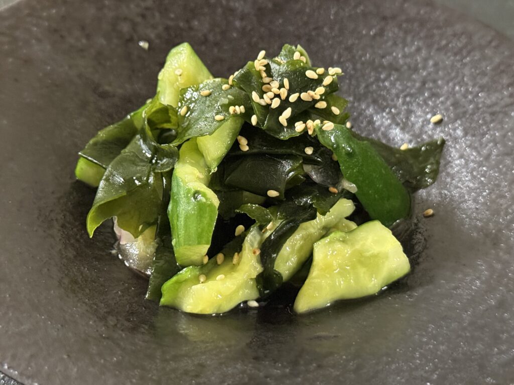 黒い器に盛られた、たたききゅうりとわかめの中華風サラダ。白ごまがトッピングされている。