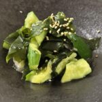 黒い器に盛られた、たたききゅうりとわかめの中華風サラダ。白ごまがトッピングされている。