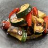 黒い器に美しく盛りつけられた、グリルしたズッキーニ、赤パプリカ、ナスなどの夏野菜。バルサミコソースが艶やかにかかっている。
