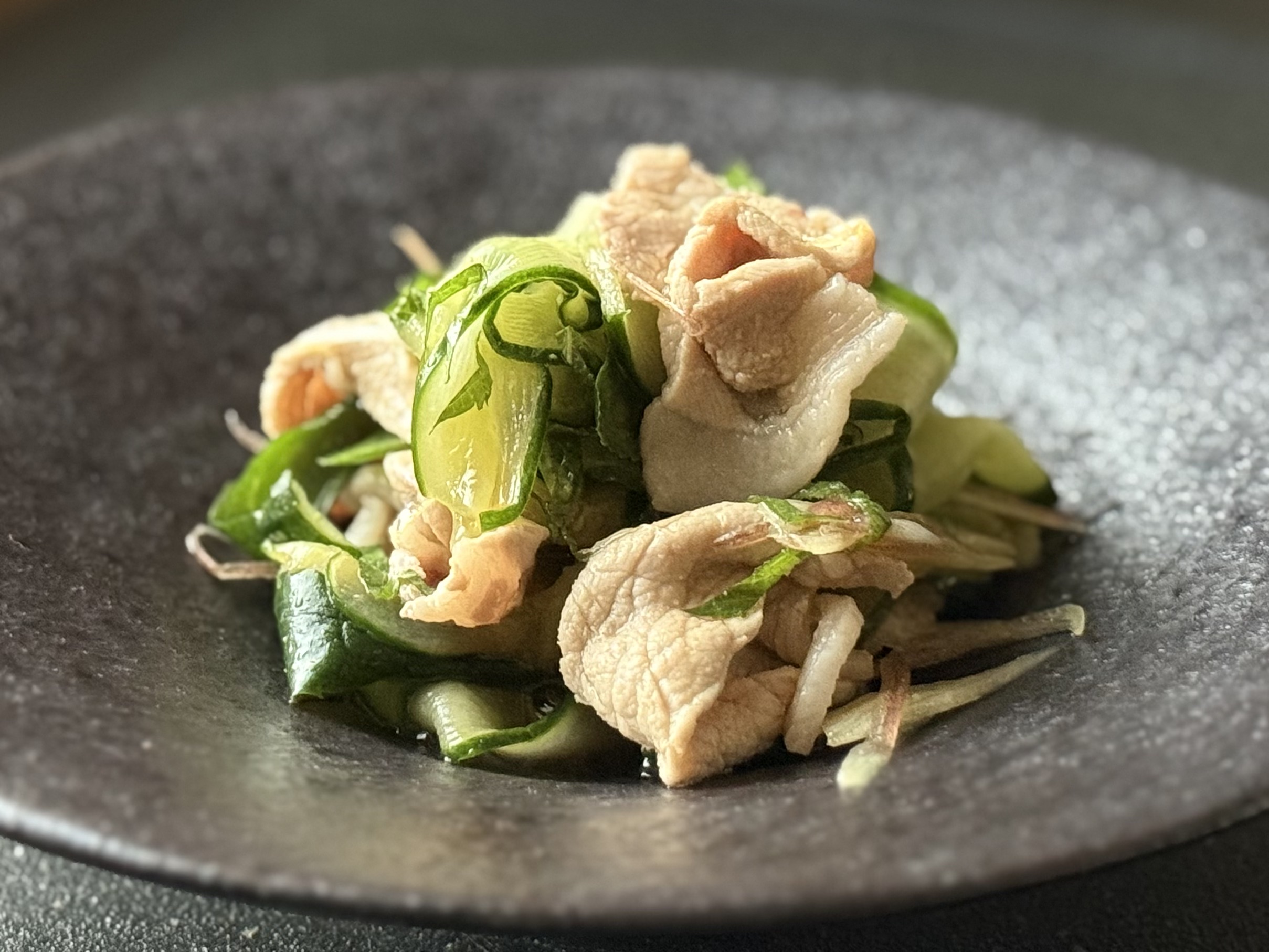 黒い器に盛りつけられた、豚しゃぶと香味野菜（ミョウガ・大葉・きゅうり）の和風サラダ。瑞々しい食感と彩りが際立つ夏の涼やかな一品。