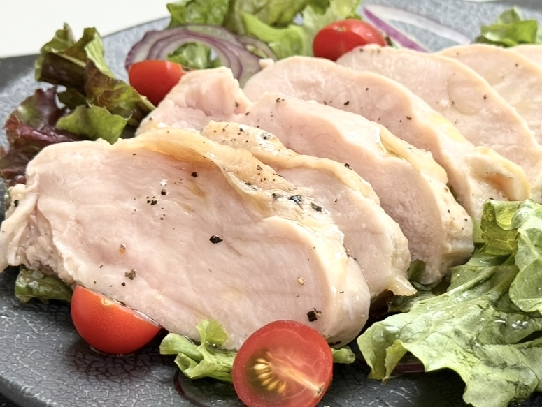 彩り野菜の上にしっとり焼かれた鶏むね肉のスライスが並ぶチキンサラダ。ミニトマトと赤玉ねぎも添えられ、やさしい塩と黒こしょうが香る一皿。