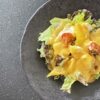 黒いプレートに盛りつけられた、黄色パプリカと豆腐のサラダ。リーフ野菜とミニトマトの上に、鮮やかなオレンジ色のドレッシングがかかっている。