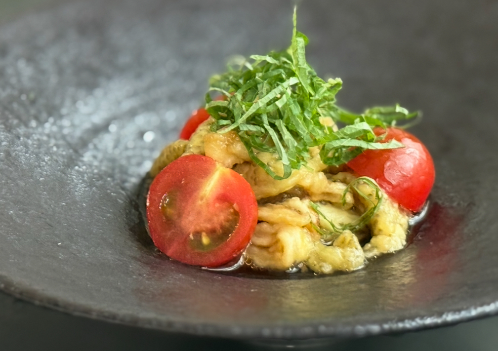 黒い器に盛られた焼き茄子とミニトマトのマリネ。千切りの大葉がトッピングされている。