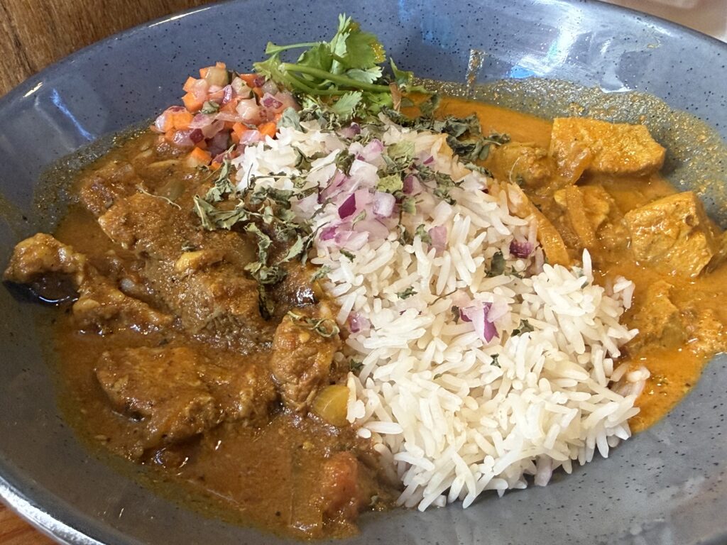 バスマティライスにパクチーと紫玉ねぎ、角切りのアチャールを添えた、アレッピーフィッシュカレーとポークビンダルーのあいがけ