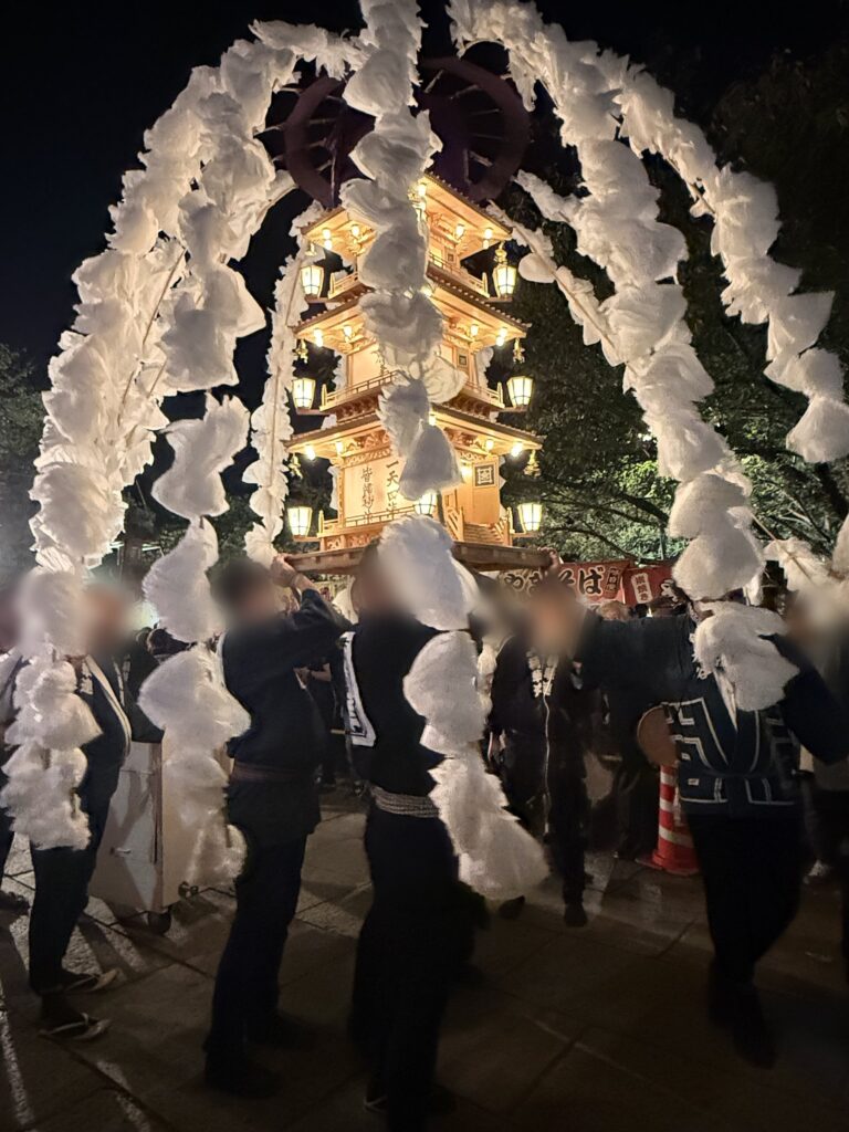 白い造花の万灯を担ぐ講中